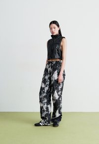 Crna kratka prsluk s visokim ovratnikom, uparen s labavim crno-bijelim hlačama u tie-dye stilu. Model nosi crne tenisice. Glatke teksture u cijelosti.