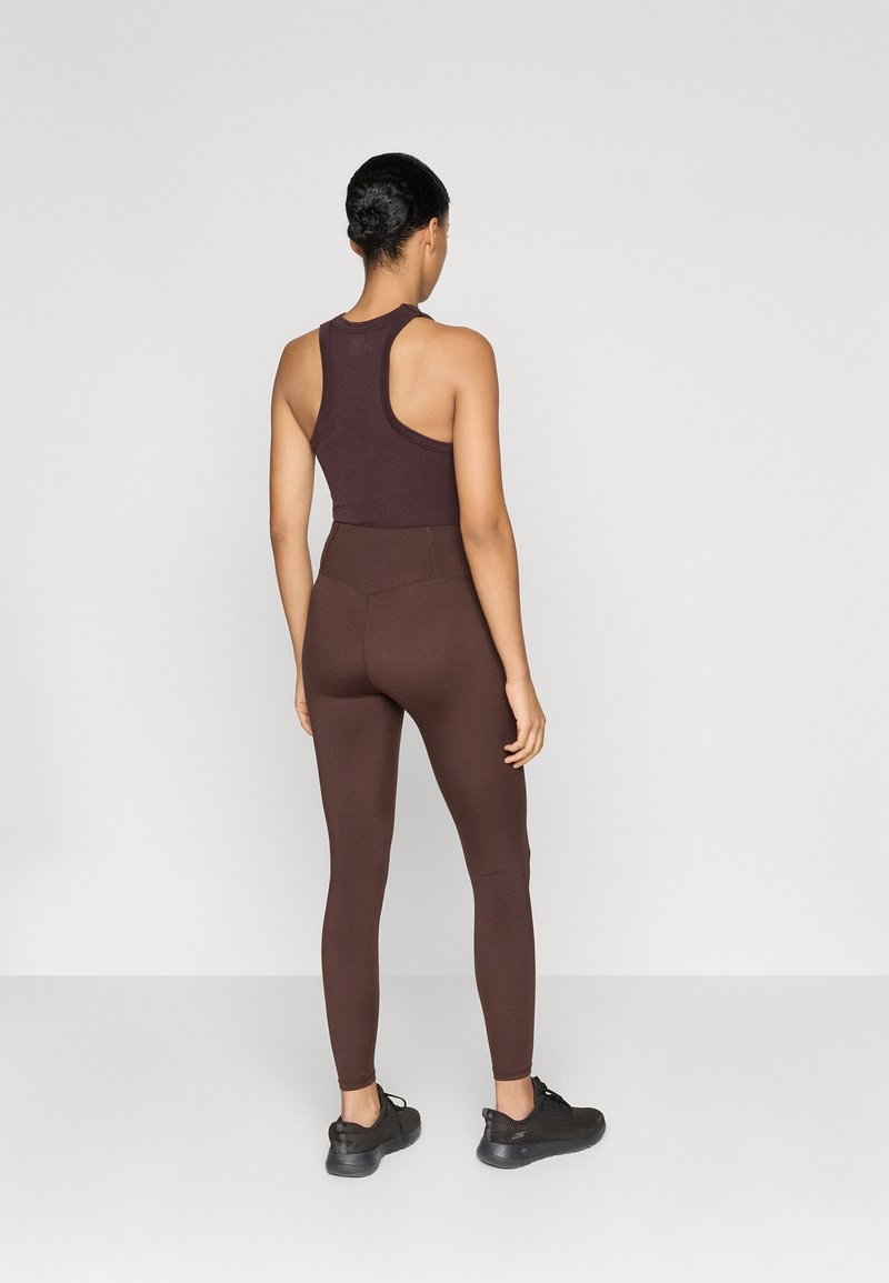 Bruine racerback sporttop en bijpassende hoge taille legging in een soepele, rekbare stof, gecombineerd met zwarte sportschoenen.