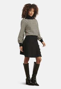 Schwarz-weißer gestreifter Pullover mit hohem Kragen, kombiniert mit einem schwarzen Rock mit seitlichen Knöpfen, ergänzt durch kniehohe schwarze Stiefel.