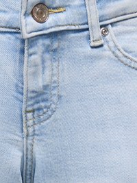 Jean en denim bleu clair en gros plan montrant une poche avant, passant de ceinture, bouton métallique, rivet et détails de couture visibles.