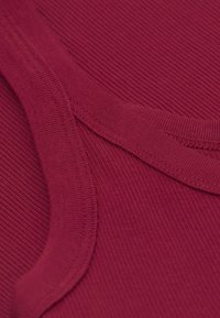 Bordeaux ribfluwelen stof met een soepele halslijn, voorzien van een subtiele textuur en contrasterende stikdetails langs de naden.