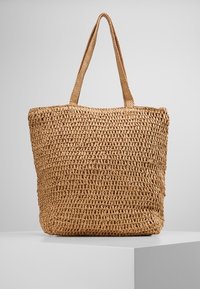 Vävd tote-väska gjord av naturliga fibrer, med rektangulär form, ljusbrun färg och två långa handtag för bärande.