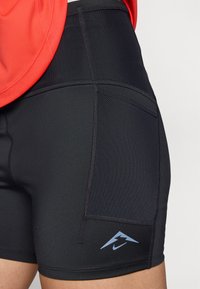 Sorte atletiske shorts med teksturert overflate, Nike-logo i blått, og en sidelomme. Livbåndet er glatt og elastisk.
