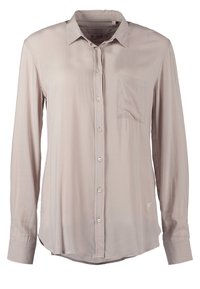 Vaaleanbeige pitkähiha-paita, joka on valmistettu sileästä kankaasta. Paidassa on klassinen kaulus, napitus edessä sekä rintatasku, jossa on hillitty kirjailu.