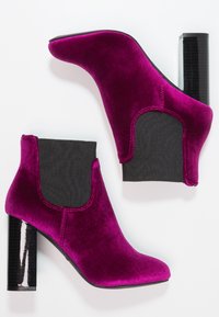Botas de tobillo de terciopelo en magenta profundo con un panel lateral de elastano negro. Presentan un tacón block negro brillante y punta afilada.