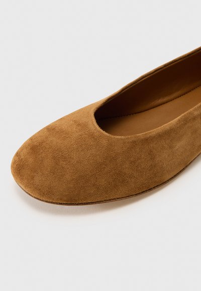 Zapato plano de ante marrón con punta redonda y una abertura amplia. Forro interior suave y diseño minimalista sin cierres visibles.