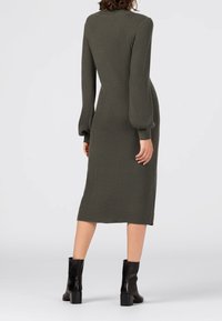Abito midi a coste verde oliva con maniche lunghe e voluminose e una silhouette aderente, abbinato a stivaletti neri.