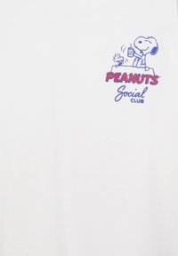 Snoopy et Woodstock assis sur une niche, Snoopy tenant un verre, avec le texte « PEANUTS Social Club » en rouge et bleu en dessous.