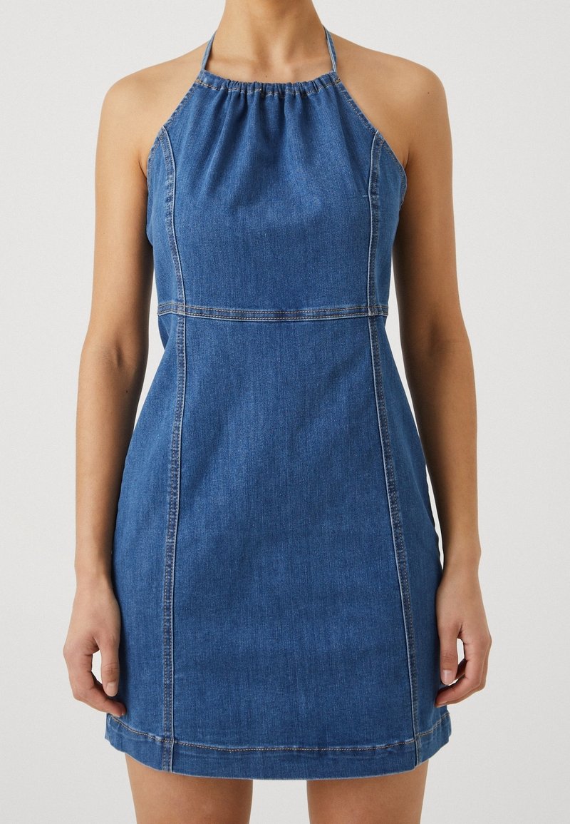 Džínové šaty se zavazováním za krkem, s přiléhavým korzetem a rozšířenou sukní. Obsahují na výstřihu nařasenou látku a kontrastní stehy.