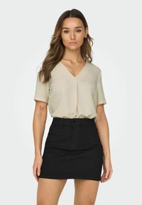 Licht beige, blouse met korte mouwen en een V-hals; gecombineerd met een strakke zwarte denimrok. De outfit heeft een soepele textuur en een casual stijl.