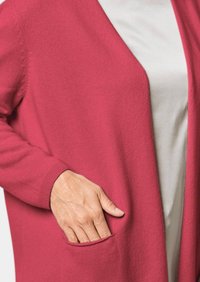 Roze cardigan gemaakt van zachte stof, met een losse pasvorm, een open voorkant en zijzakken. Voorzien van geribbelde manchetten voor extra detail.