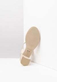 Sandale beige avec un dessus lisse et brillant, des fines lanières et un talon carré de hauteur moyenne. Semelle en caoutchouc texturé avec une marque embossée.