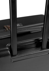 Black hard-shell suitcase with dual retractable handles, side zipper, combination lock, and textured surface for grip.