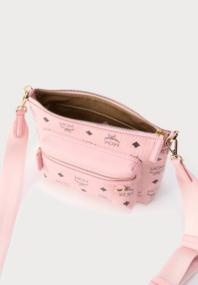 Ροζ τσάντα χιαστή με μαύρα λογότυπα MCM, χρυσά μεταλλικά στοιχεία, μπροστινή τσέπη με φερμουάρ και ρυθμιζόμενο υφασμάτινο λουράκι, εμφανιζόμενη ανοιχτή για να αποκαλύψει την εσωτερική επένδυση.
