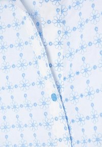 Blå och vit blommönstrad skjorta i bomullstyg, med små blå knappar och en detaljerad sömdesign av blommor och prickar.