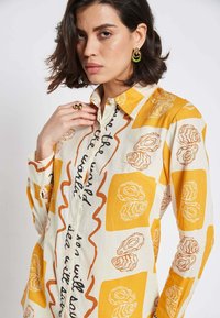 Long-sleeve shirt in lightweight fabric featuring a yellow and cream oyster pattern with decorative text. Button-down collar and relaxed fit.