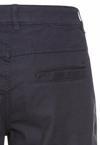 Un pantalon en coton bleu foncé présente une texture lisse, une coupe droite et une poche arrière avec un rabat simple. Des coutures sont visibles.