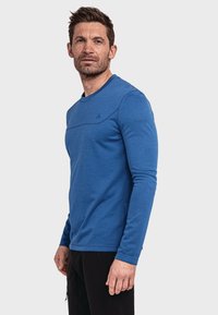 Langärmliges blaues Sportshirt mit rundem Halsausschnitt, strukturiertem Stoff und einer horizontalen Naht über der Brust. Minimale Markenkennzeichnung sichtbar.