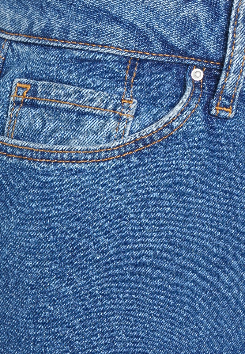 Detailní záběr na denní látku v světlomodré barvě, s výrazným oranžovým prošitím a malou přední kapsičkou s kovovým nýtem.