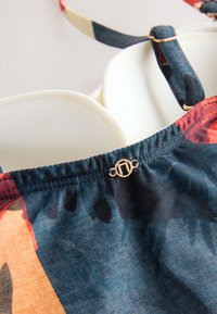 Kolorowy kwiatowy strój kąpielowy z usztywnianymi miseczkami, regulowanymi ramiączkami oraz ozdobnym złotym detalem na środku z przodu.