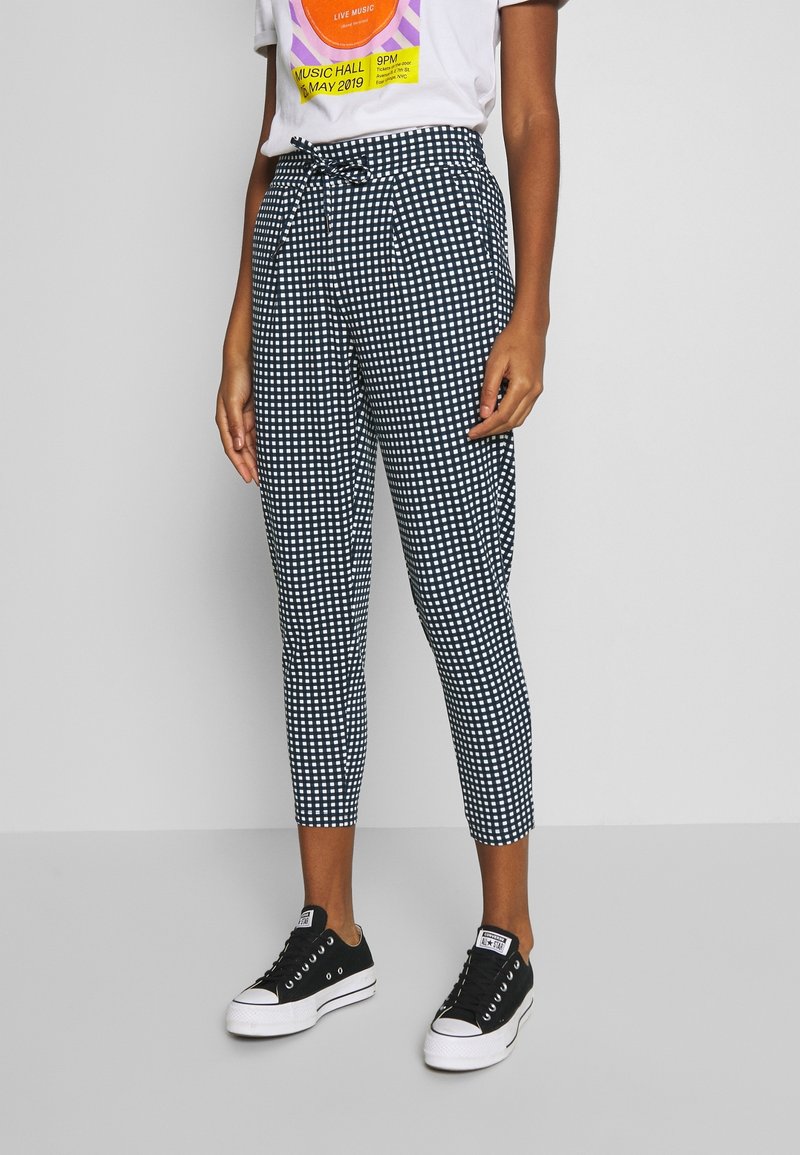 Czarno-białe spodenki w kratę z dopasowanym stanem i skróconą długością, wykonane z lekkiego materiału, w połączeniu z czarnymi sneakersami.