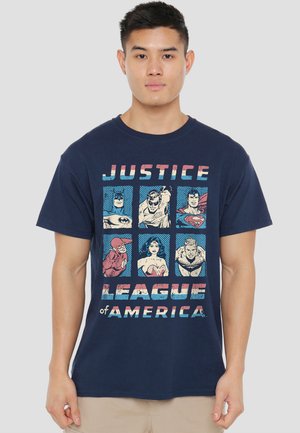 Young man wearing navy blue Justice League of America T-shirt featuring six comic-style superhero portraits in a 2x3 grid.