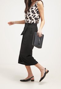 Černé culottes s páskem v pase, doplněné světle růžovým topem se geometrickým černým vzorem. Celkový vzhled doplňují černá kabelka a ploché sandály.