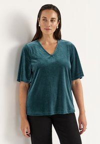 Tealfärgad sammetslik kortärmad topp med V-ringning. Mjuk textur, avslappnad passform och slät finish. Matchad med svarta byxor.