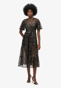 Vestido negro de midi con lentejuelas, mangas cortas onduladas, cuello redondo y falda de capas. Presenta una superposición transparente y un forro suave.