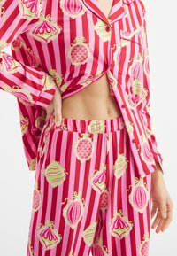 Conjunto de pijama a rayas rosas y rojas con patrones en forma de concha en verde y rosa. La tela es suave, con un corte holgado y cintura elástica.