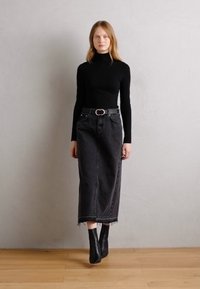 Top negru cu guler înalt, combinat cu o fustă din denim neagră, cu talie înaltă, având un tiv desfăcut. Modelul poartă cizme negre până la gleznă și o curea cu o cataramă argintie.