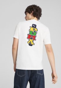 Camiseta blanca de manga corta con un diseño del logo 'PUMA' multicolor en la parte posterior, que presenta letras en rojo, verde, amarillo y azul.
