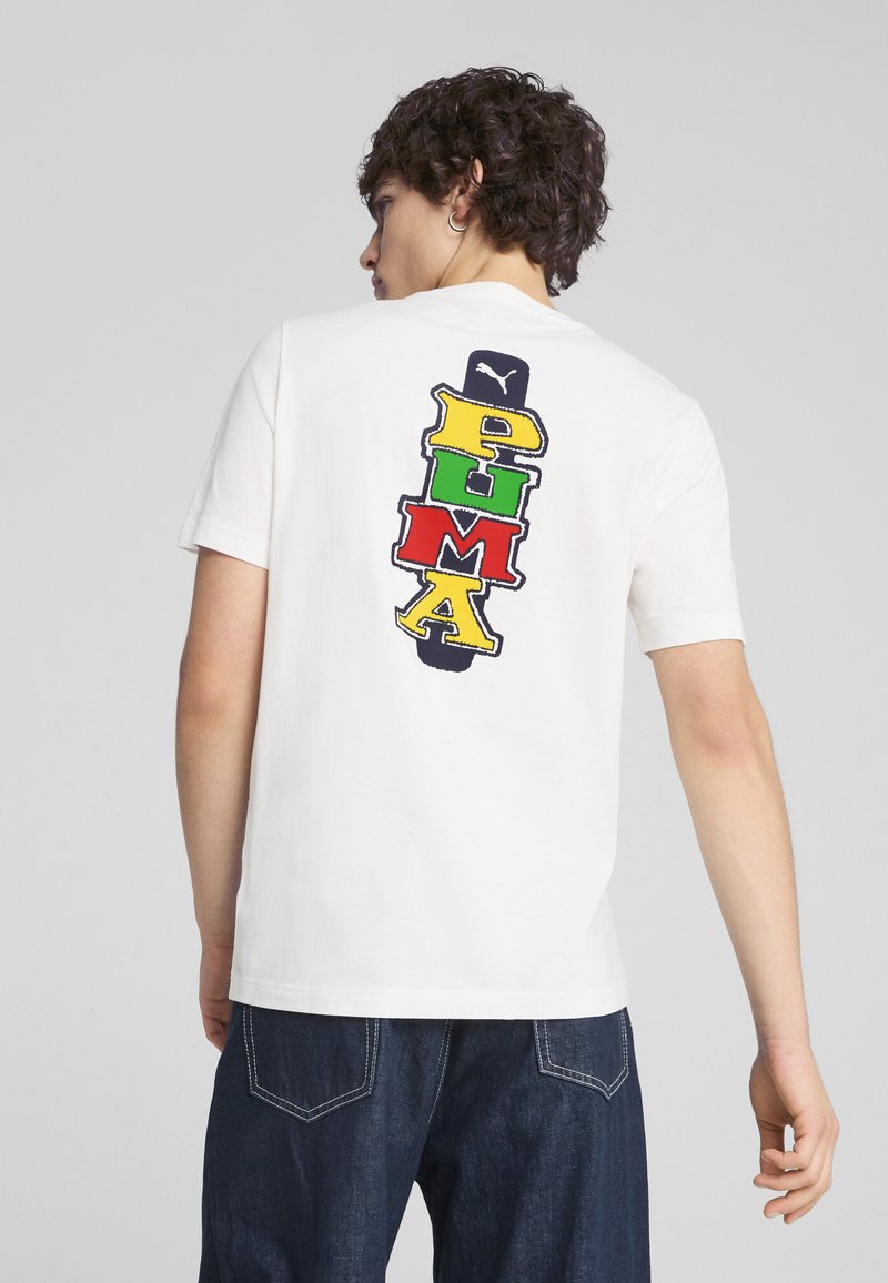 Camiseta blanca de manga corta con un diseño del logo 'PUMA' multicolor en la parte posterior, que presenta letras en rojo, verde, amarillo y azul.