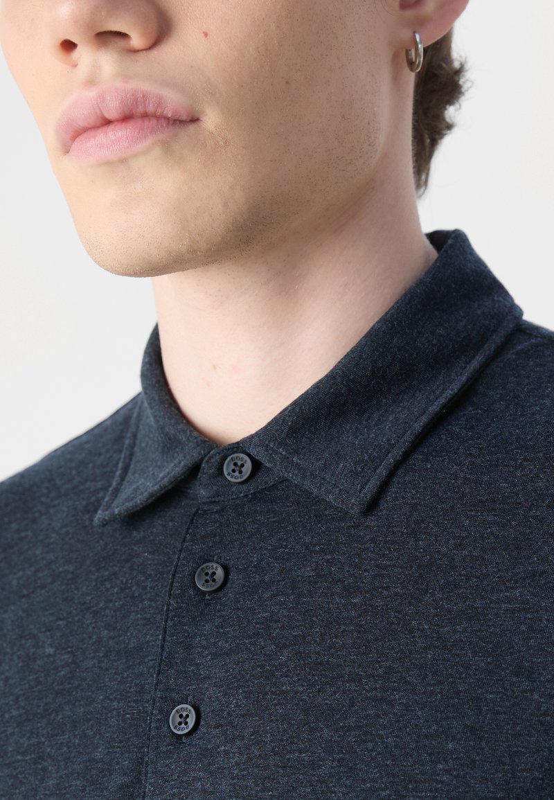 Dunkelmarineblaues Poloshirt mit weicher Textur, klassischem Kragen und drei schwarzen Knöpfen auf der Vorderseite.