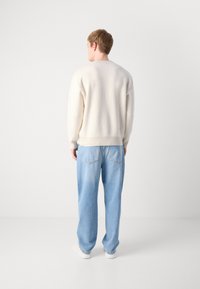 Ecru-gestreifter Pullover mit Rundhalsausschnitt, kombiniert mit hellblauen, locker sitzenden Jeans. Das Outfit wird mit weißen Sneakern abgerundet.