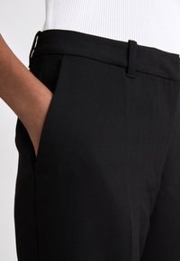 Pantaloni negri, croiți, cu o textură netedă, având un talie simplă, buzunare laterale și un design ajustat.