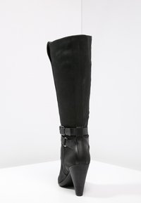 Botte noire montant jusqu'au genou avec un dessus en tissu texturé, des accents en cuir lisse, un talon aiguille et deux détails de boucle sur le côté.