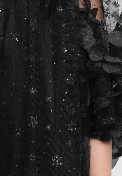 Crni til tkanina ukrašena srebrnim cvjetnim uzorcima i šljokicama, s naboranim detaljima sa strane za teksturu i dubinu.