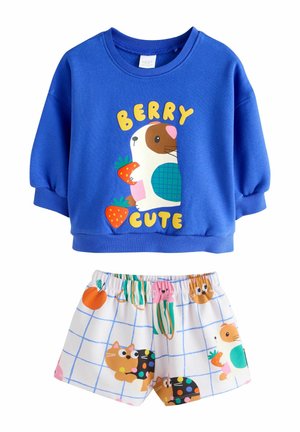 Niebieska bluza z napisem „Berry Cute” i świnką morską trzymającą truskawki, połączona z białymi szortami z kolorowymi wzorami kotów i owoców.