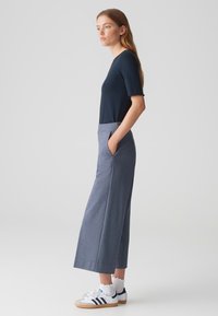 Haut ajusté bleu marine à manches courtes ondulées, associé à un large pantalon gris-bleu avec poches latérales et des baskets blanches avec des rayures bleu marine.