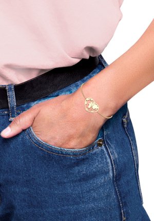 Goldfarbenes, herzförmiges Armband mit einem Weltkartenmuster, das durch eine zarte Kette verbunden ist. Es wird an einer Hand getragen, die in einer Jeans-Tasche ruht.