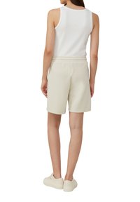 Helle graue Shorts aus einem weichen Material mit einem elastischen Bund und einem lockeren Schnitt. Kombiniert mit einem weißen Tank-Top und lässigen Sneakers.