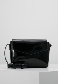 Borsa a tracolla in pelle verniciata nera con chiusura a pattina, design angolare, tracolla regolabile e finitura lucida. Forma compatta e rettangolare.