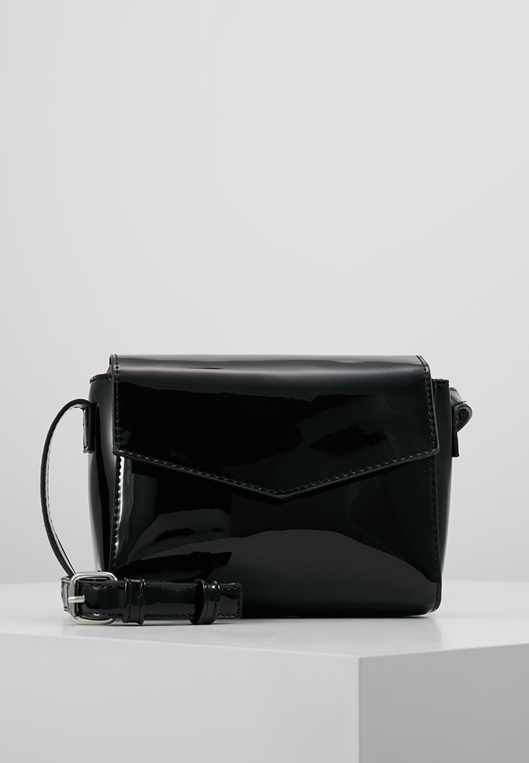 Borsa a tracolla in pelle verniciata nera con chiusura a pattina, design angolare, tracolla regolabile e finitura lucida. Forma compatta e rettangolare.