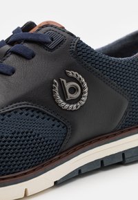 Navyblaue Sneakers aus Leder und Mesh, mit strukturiertem Obermaterial, braunen Akzenten und einem silbernen Logodetail an der Seite.