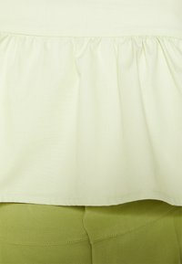 Top verde claro com bainha franzida, tecido texturizado; combinado com parte inferior verde oliva de cintura alta, com costuras planas e acabamento suave.