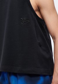 Gros plan d'une personne portant un débardeur noir avec un petit logo Nike et un short bleu.