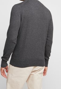 Pull gris tricoté avec col rond et manches longues. Tissu texturé avec poignets et ourlet côtelés. Style avec un pantalon de couleur claire.