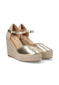 Espadrilles en cuña metálica dorada con correas de tela trenzada, suelas envueltas en yute y borde ondulado en la punta. Correa ajustable en el tobillo incluida.