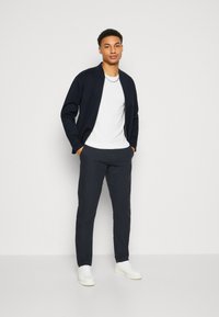 Navy bomber jacket over a white t-shirt, paired with dark pants and white sneakers. The outfit features a minimalistic design.